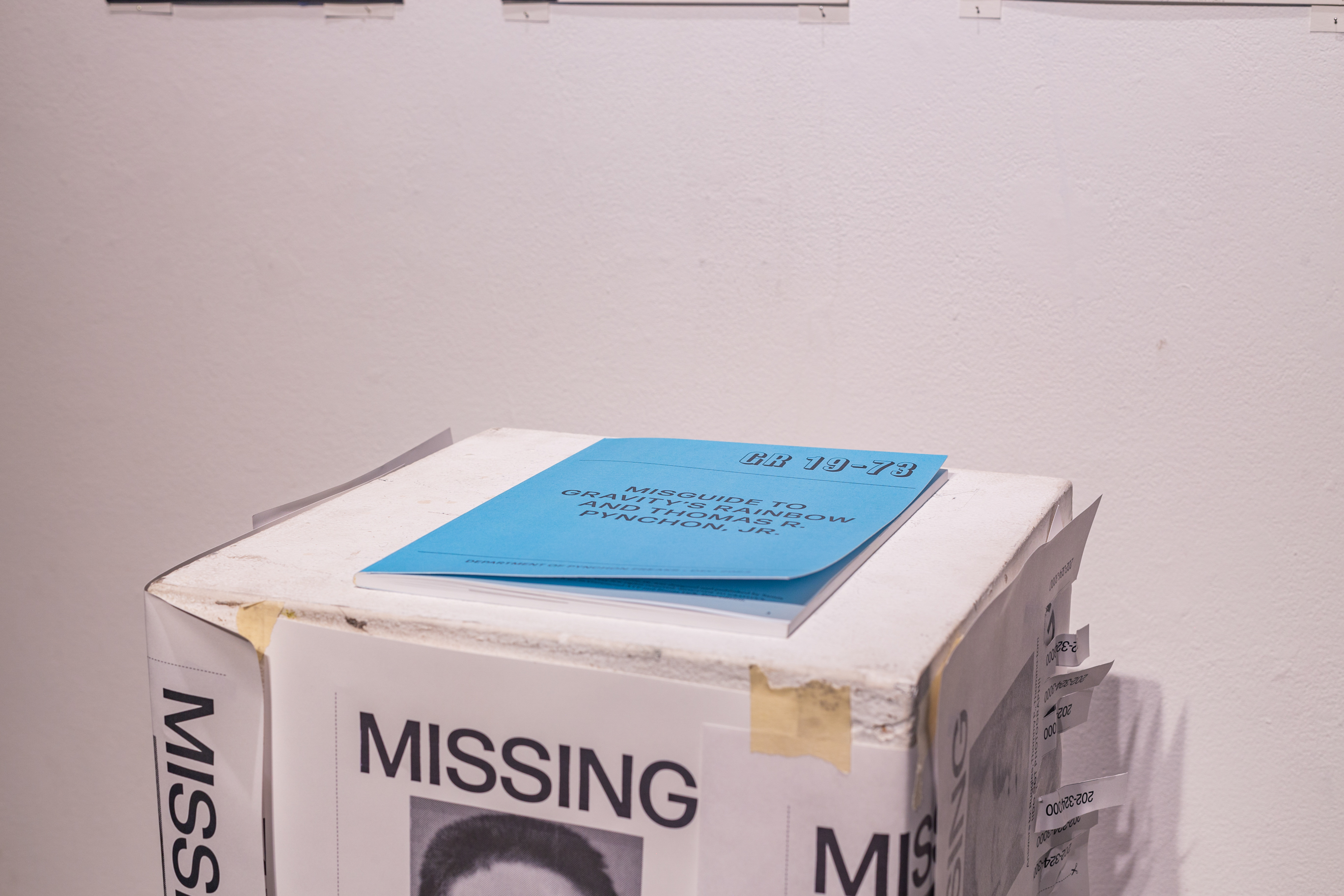 A podium with multiple fabricated missing person posters. On the podium is a book.